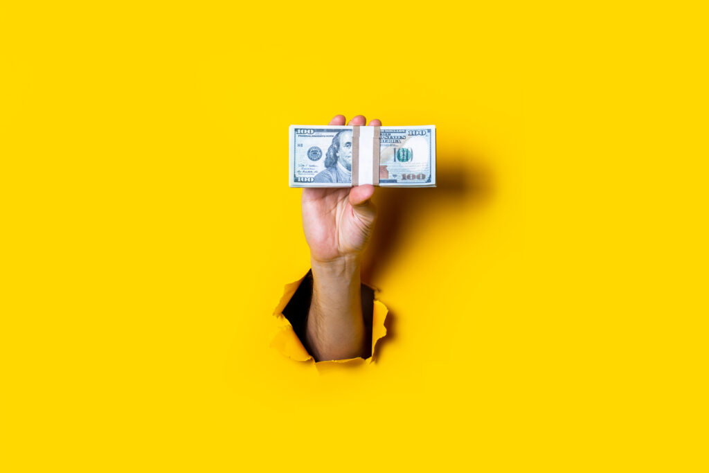 Female hand holds horizontally a bundle of money bills on a yellow background - Trade Info skúsenosti, trh