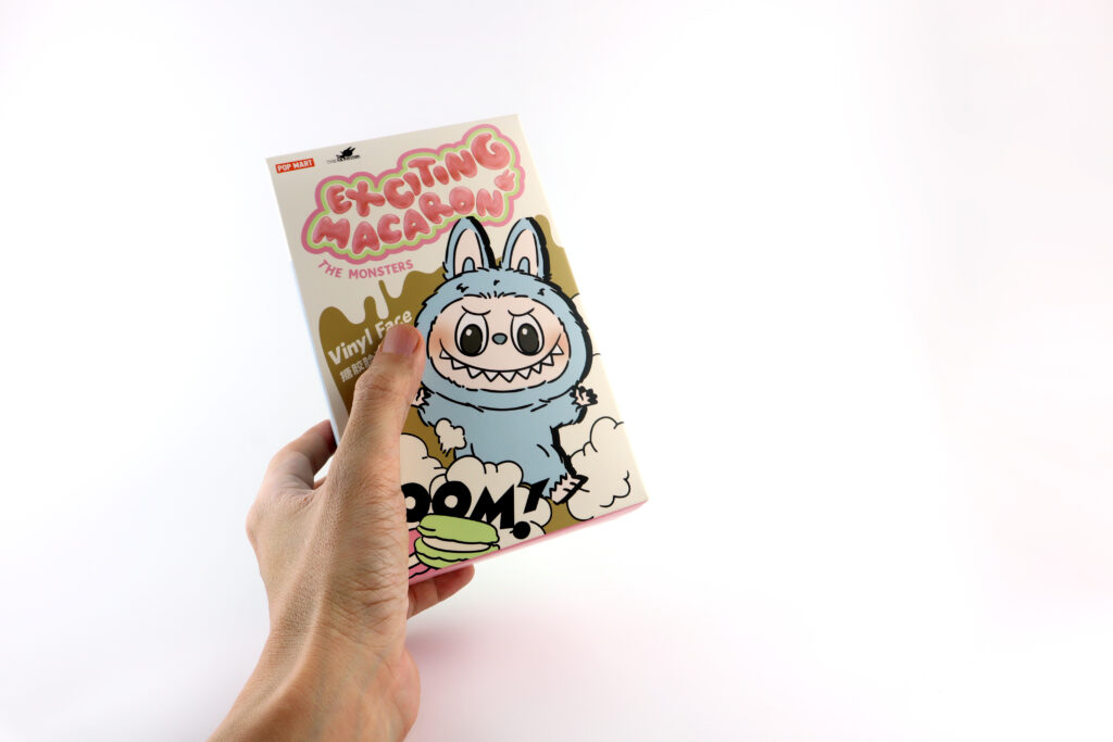 left hand holding an art toys Labubu key chain box package paccollection from Pop Mart blind box collectable cute toys white background at Pop mart store during new release event labubu macaron doll - Trade Info LABUBU, figúrky, bizarné