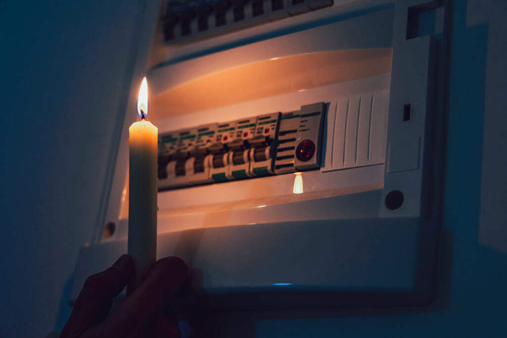 Energy crisis Hand in complete darkness holding a candle to investigate a home fuse box during a power outage Blackout concept - Trade Info blackout