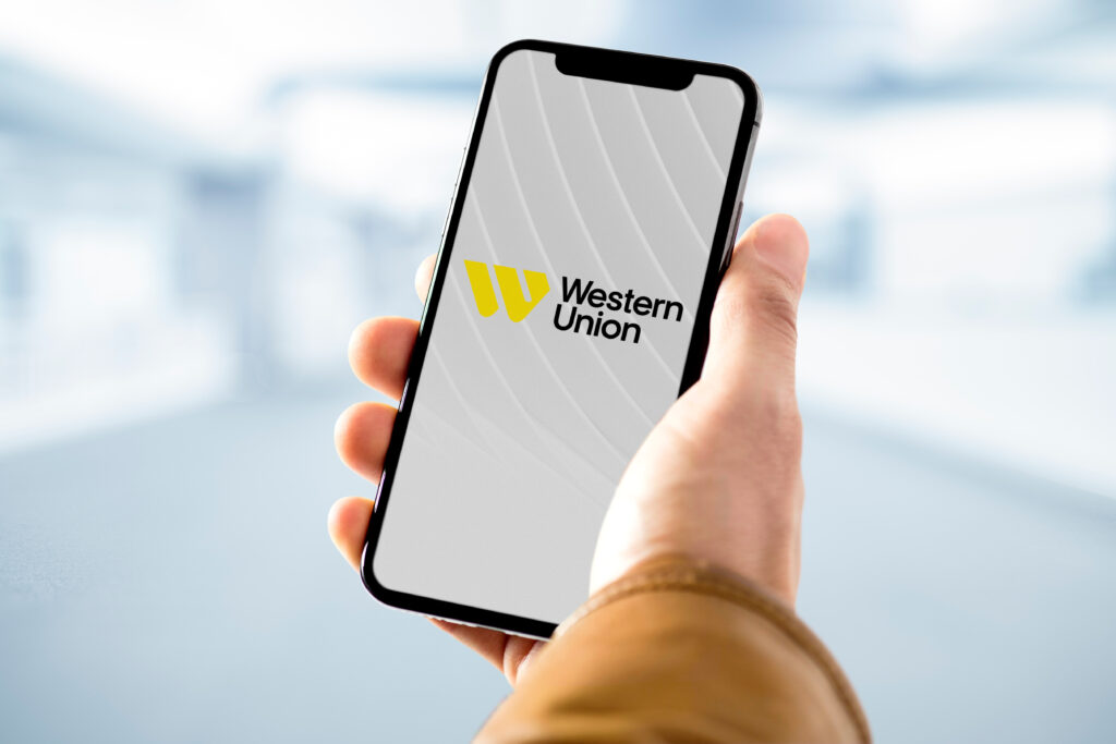 Businessman holding smartphone with western union logo on screen - Trade Info Western Union, digitálne prevody, krypptomeny, kryptomen