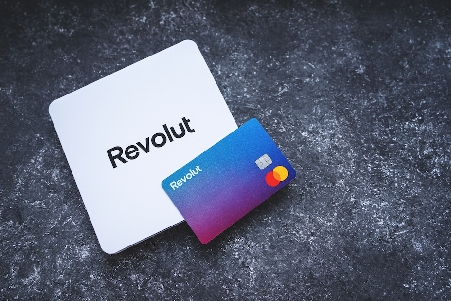 Revolut gradient blue-to-pink card beside a white Revolut box on a dark textured surface with Mastercard logo visible.