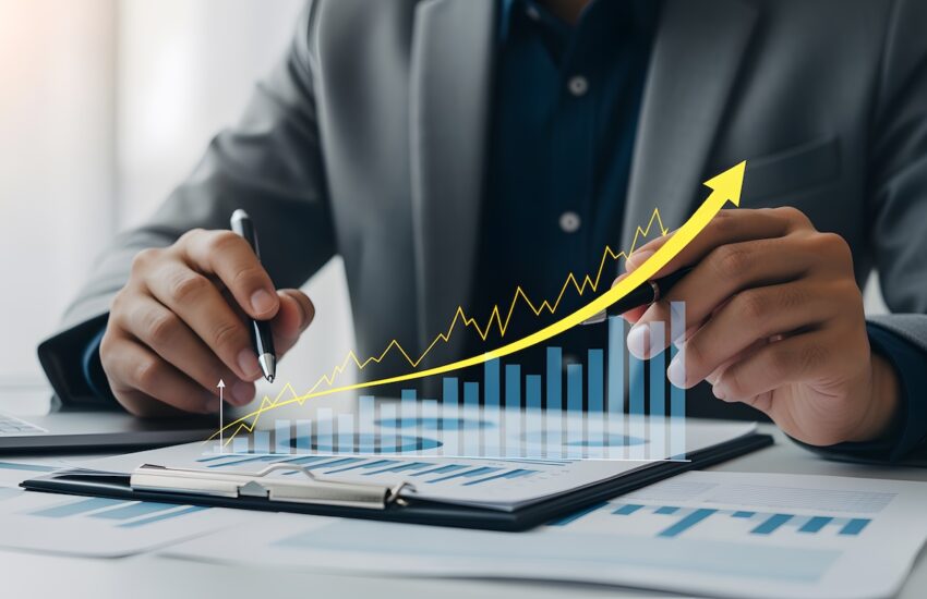 Businessperson in a suit analyzes financial charts, with a glowing yellow upward-trend arrow over blue bar graphs on a clipboard and documents.