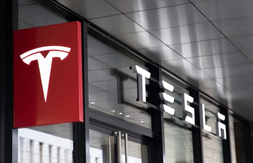 Tesla storefront sign: red square panel with white Tesla T logo beside glass doors