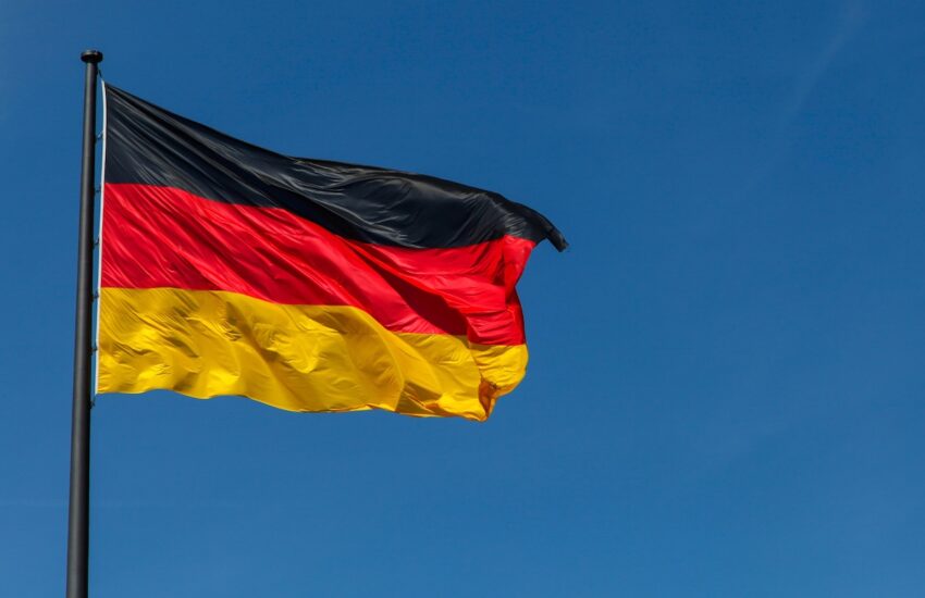 German flag waving on a tall flagpole against a clear blue sky