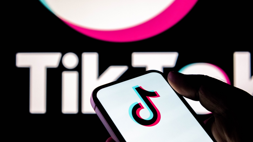 Phone screen shows the TikTok logo while a bright TikTok wordmark appears in the background, suggesting the app brand.