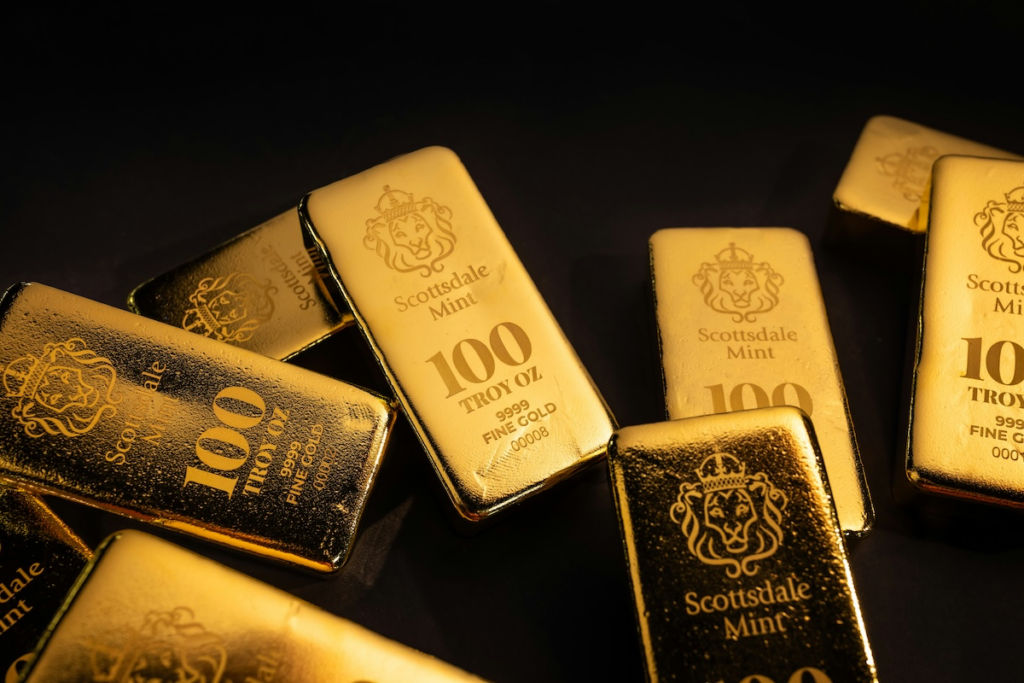 image - Trade Info Gold bars scattered on a dark surface, labeled Scottsdale Mint, 100 troy oz, .999 fine gold (various bar orientations).